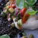 Close-up of a gourmet fish fillet with lentils, tomato, and fresh herbs on a plate.